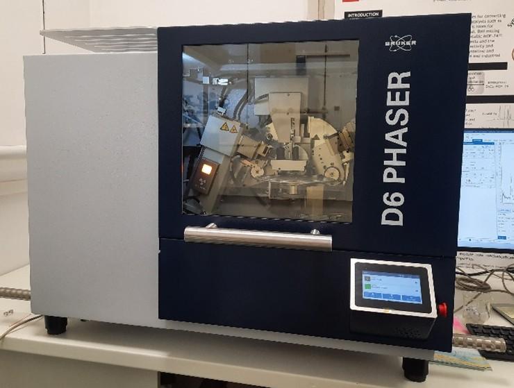 Slika difraktometra, sivo-modri instrument oblika kocke sa prozorom i metalnom ručkom na prednjoj strani. Pokraj prozora piše D6 PHASER, a kroz prozor se vidi unutrašnjost instrumenta s raznim svjetlima i metalnim pomičnim djelovima. Na prednjoj strani instrumenta vidi se mali ekran, a s desne strane instrumenta vidi se upravljačko računalo